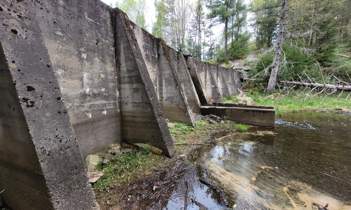 Mur en béton d’un barrage ancien visible en bord de cours d’eau, intégré dans un environnement forestier à Victoriaville